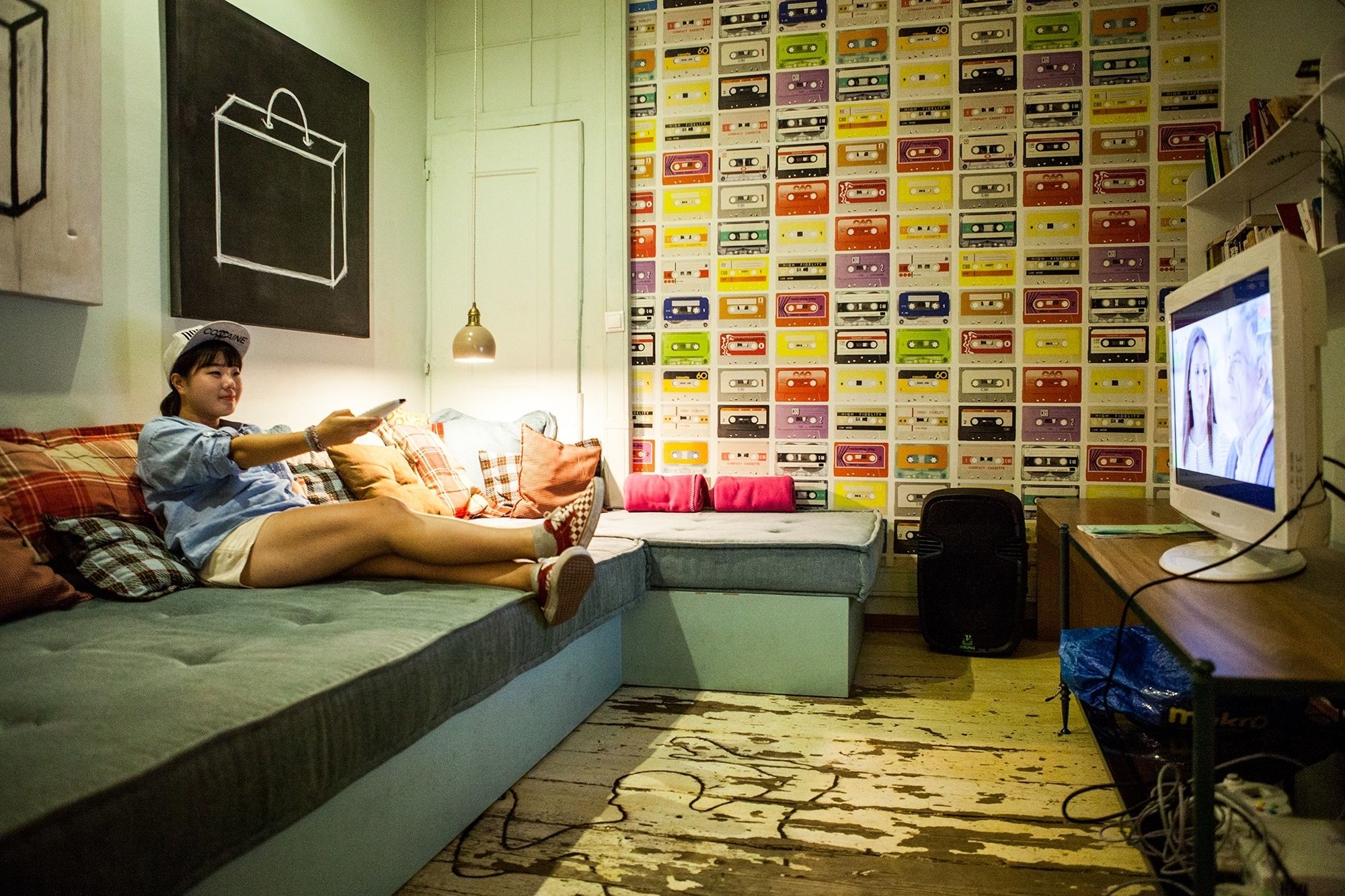 Una habitación con sofá, televisión y una pared cubierta de cintas de cassette de colores.