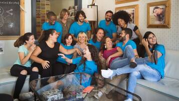 A group of people sitting on a couch and a coffee table in a room with a white wall and framed pictures.