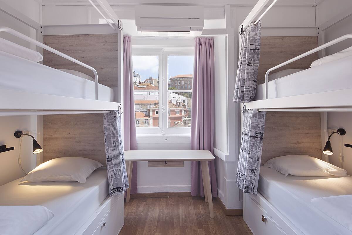 A dormitory room with bunk beds, a desk, and a window with curtains.