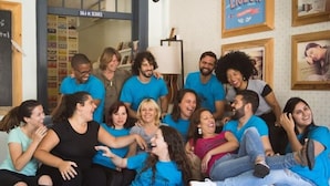 A group of people sitting on a couch in a room with a bookshelf and a sign that reads "I Love Lisbon".