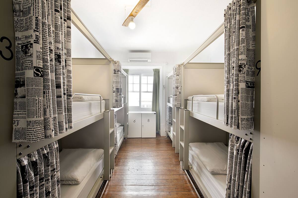 A narrow hallway with bunk beds on either side, a wooden floor, and a door at the end.