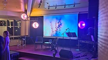 An indoor venue with a stage, seating, and a large screen.
