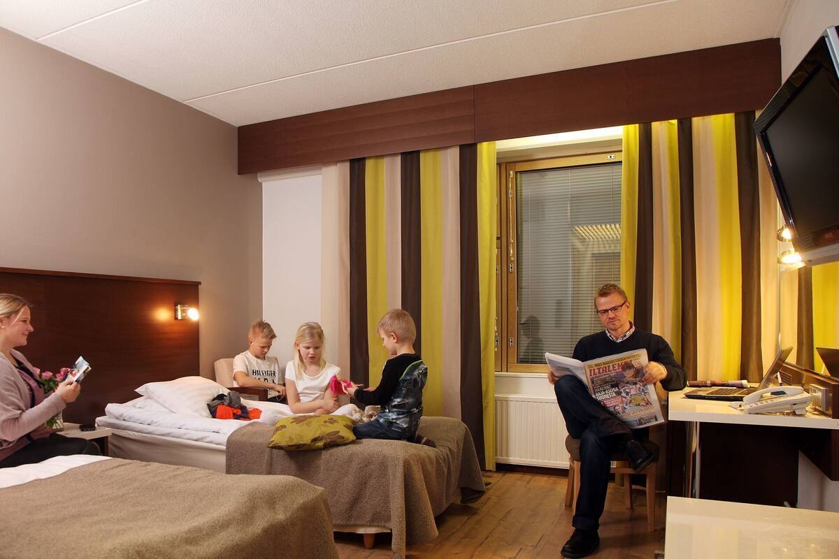 Una habitación de hotel con cama, un escritorio con computadora portátil y ventana con cortinas.
