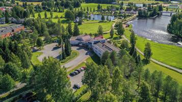 An aerial view of a hotel with a parking lot, a river, and surrounding greenery.