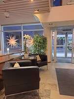 Um lobby moderno com entrada por porta de vidro, decoração em forma de estrela, planta em vaso e área de estar com mesa de vidro.