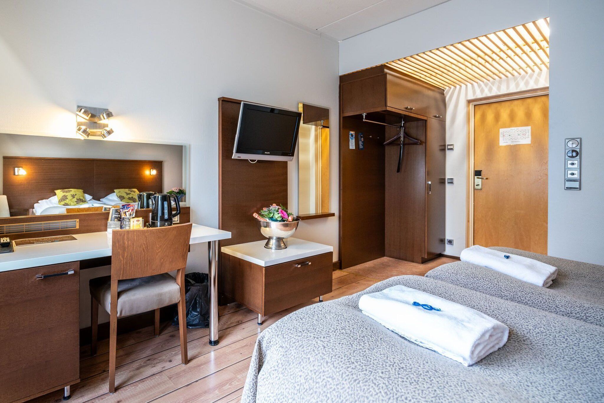 A hotel room with a bed, a desk with a chair, a television, a wardrobe, and a shower area.