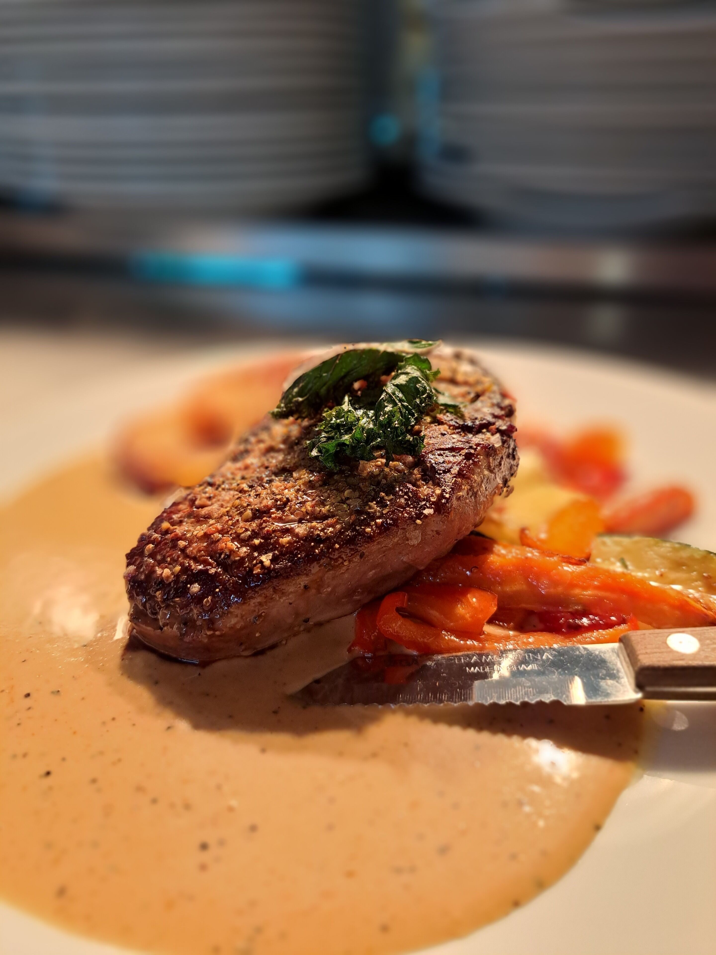 A steak with a garnish on a plate with vegetables and sauce.