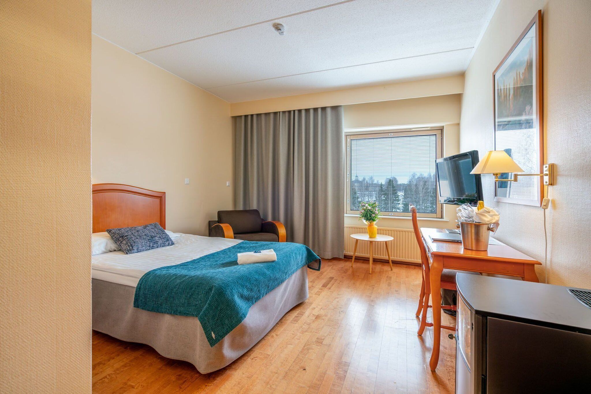 Habitación de hotel con cama, escritorio, silla, televisión y ventana con cortinas.