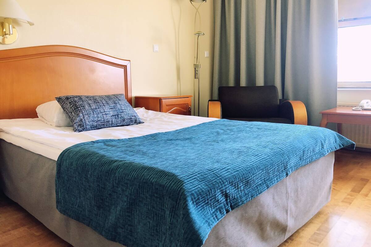Una cama bien hecha con una manta azul, un cabecero de madera y un almohadón gris.