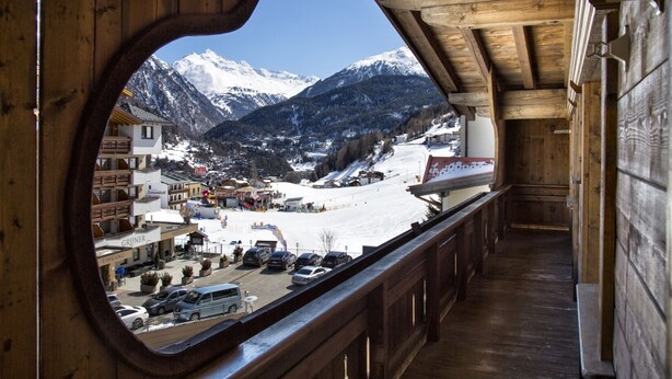 A wooden interior with a large window overlooking a snowy mountain landscape, including a ski resort and buildings. - A CASA Juwel - Ski in & Out Appartements (Soelden)