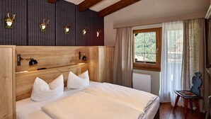 A bedroom with a wooden headboard, a large bed with white bedding, a nightstand, a lamp, a window with curtains, and a view of the outdoors. - A CASA Juwel - Ski in & Out Appartements (Soelden)