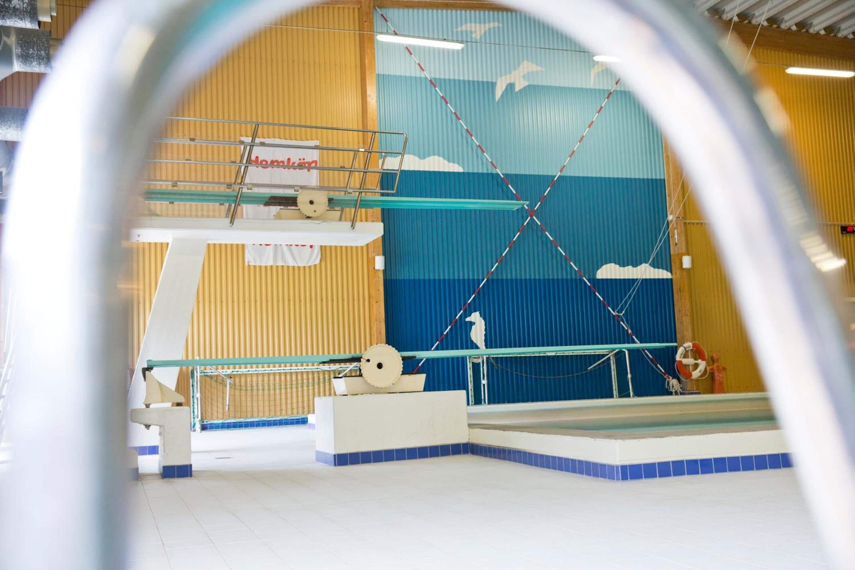 Una piscina interior con una plataforma de salto, un flotador salvavidas y un mural en la pared.