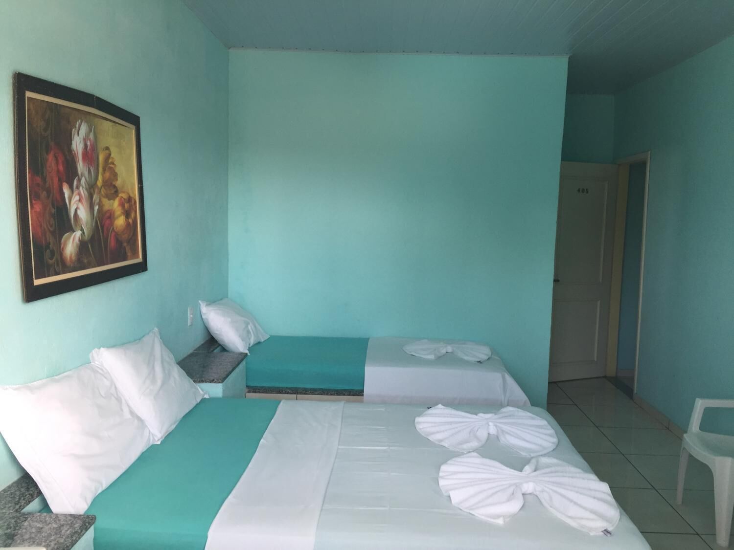 Quarto de hotel com duas camas, um quadro na parede e uma porta à direita.