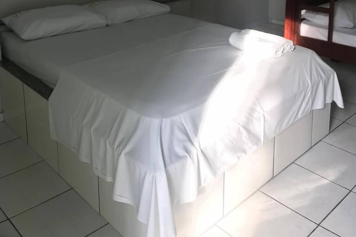 A single bed with a white bedspread, a wooden bunk bed to the right, and a framed floral artwork on the wall.