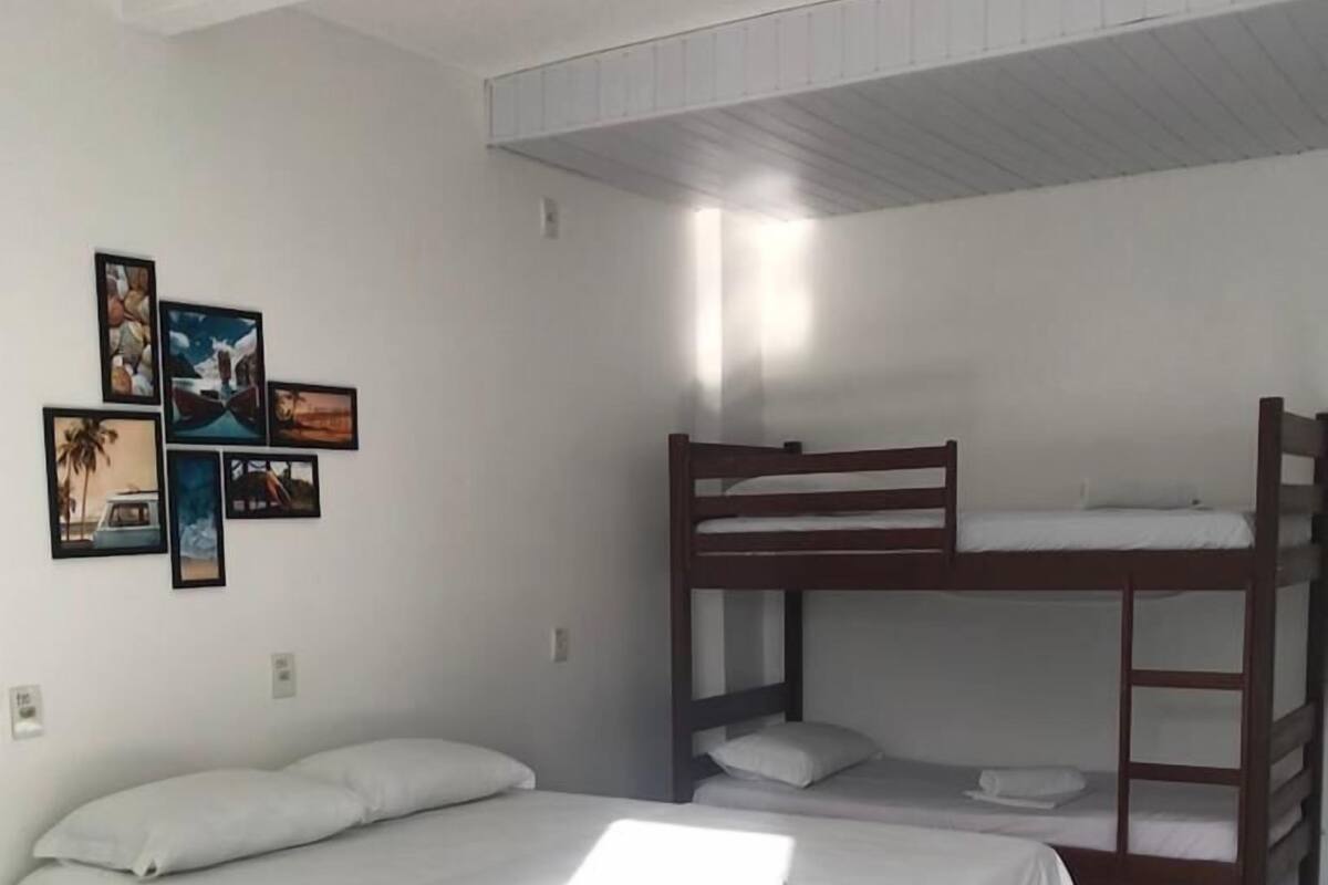 A room with a bunk bed, a single bed, and a wall with framed pictures.