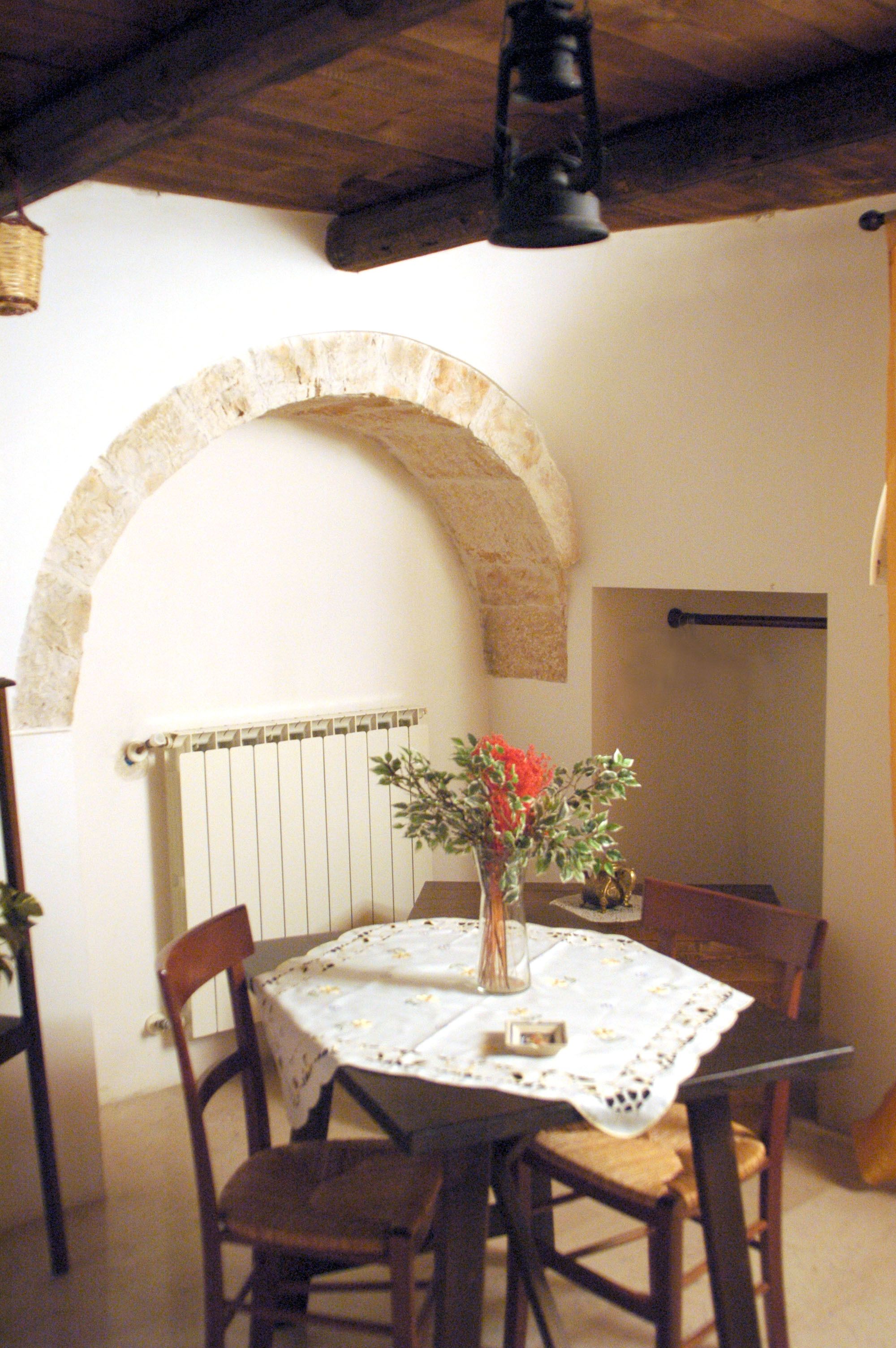 A dining area with a round table, chairs, a vase with flowers, and a stone archway.