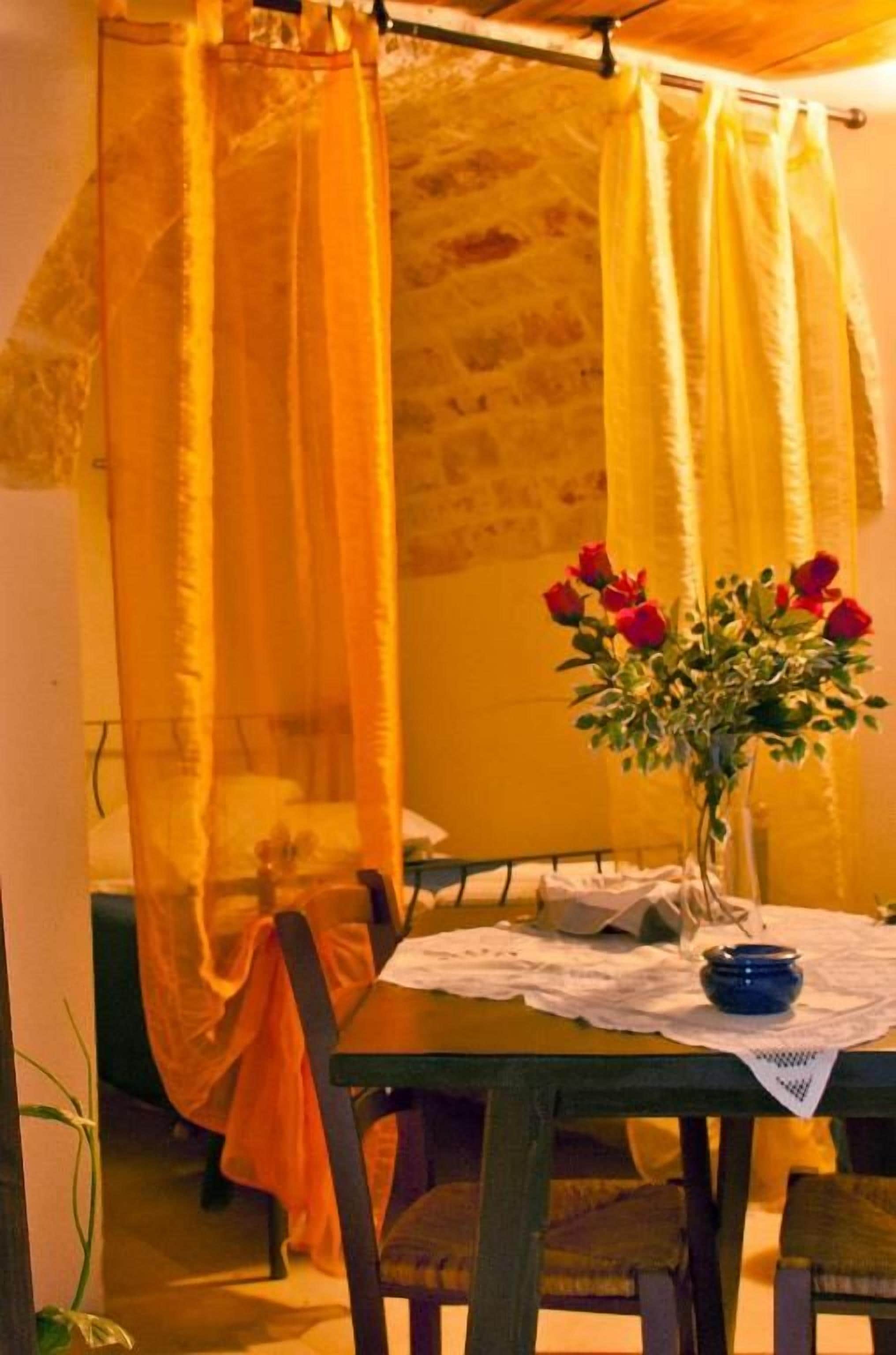 Una habitación con una cama cubierta por un dosel amarillo, una mesa con un florero de flores rojas y una silla.
