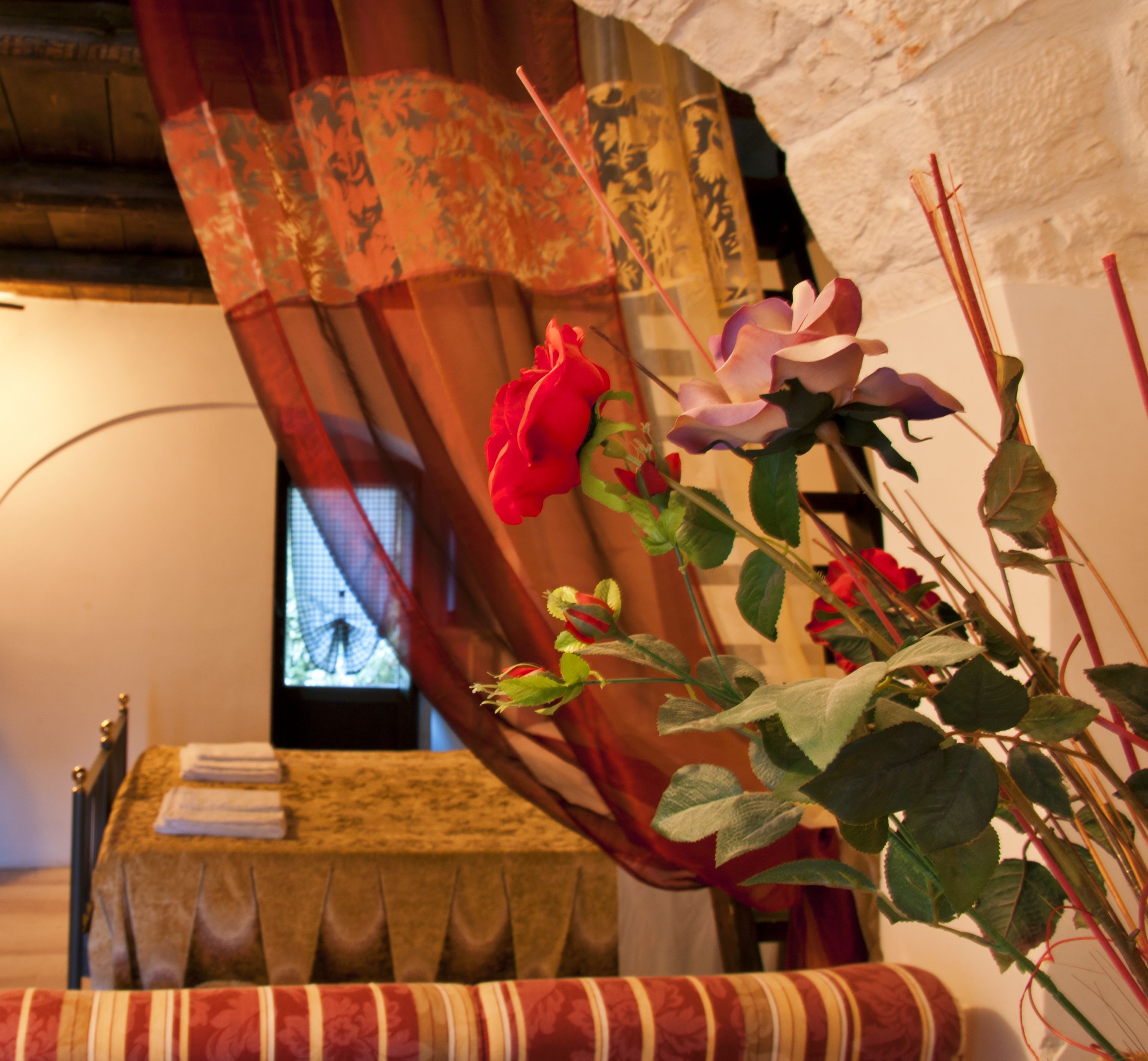 A room with a bed, a window with curtains, and a plant with flowers.
