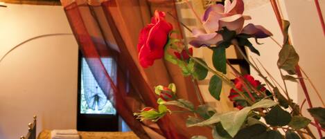 A room with a bed, a window with curtains, and a plant with flowers.