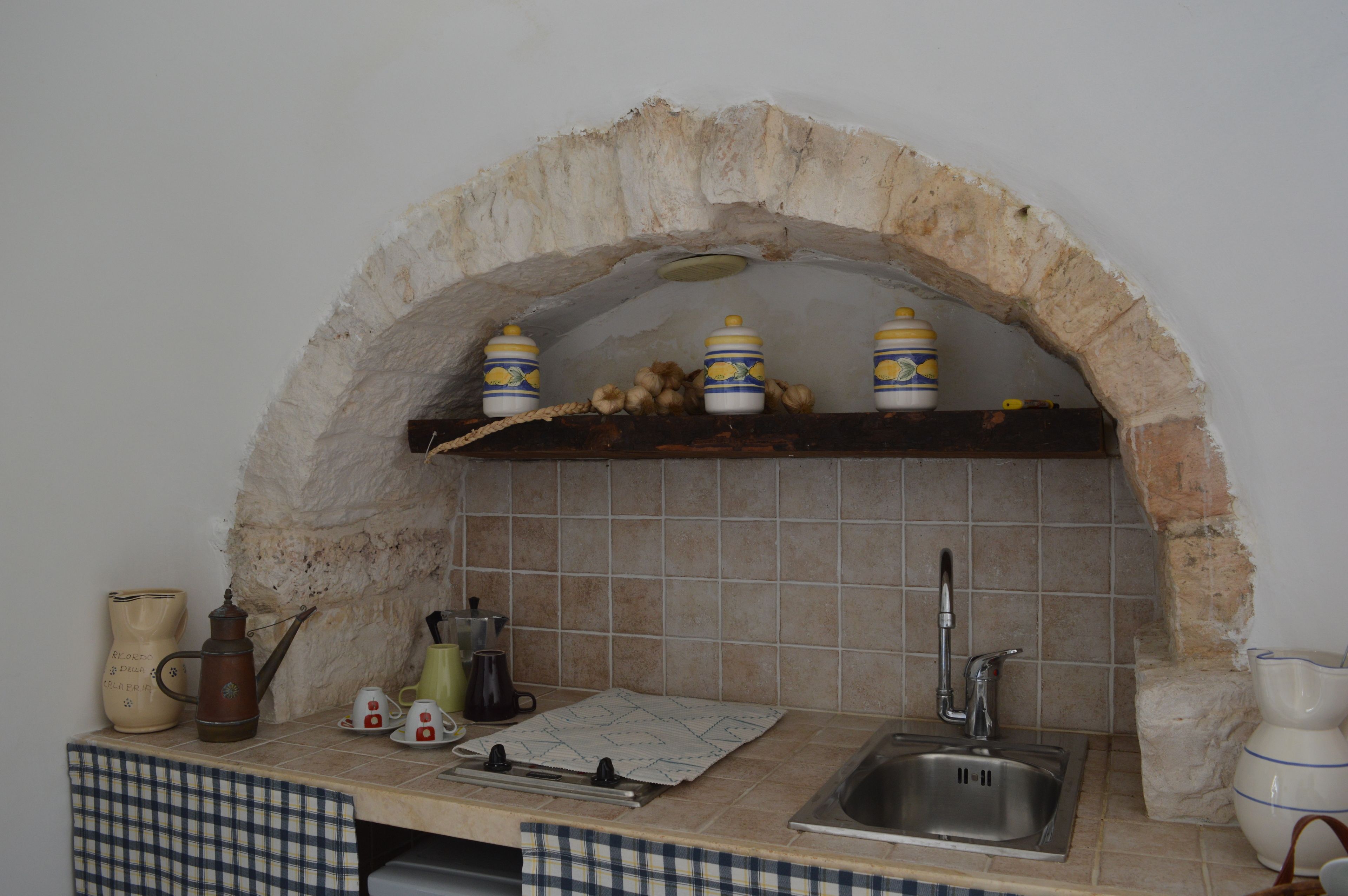 Cucina con arco in pietra, lavello e diversi utensili da cucina.