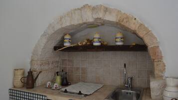 Cucina con arco in pietra, lavello e diversi utensili da cucina.
