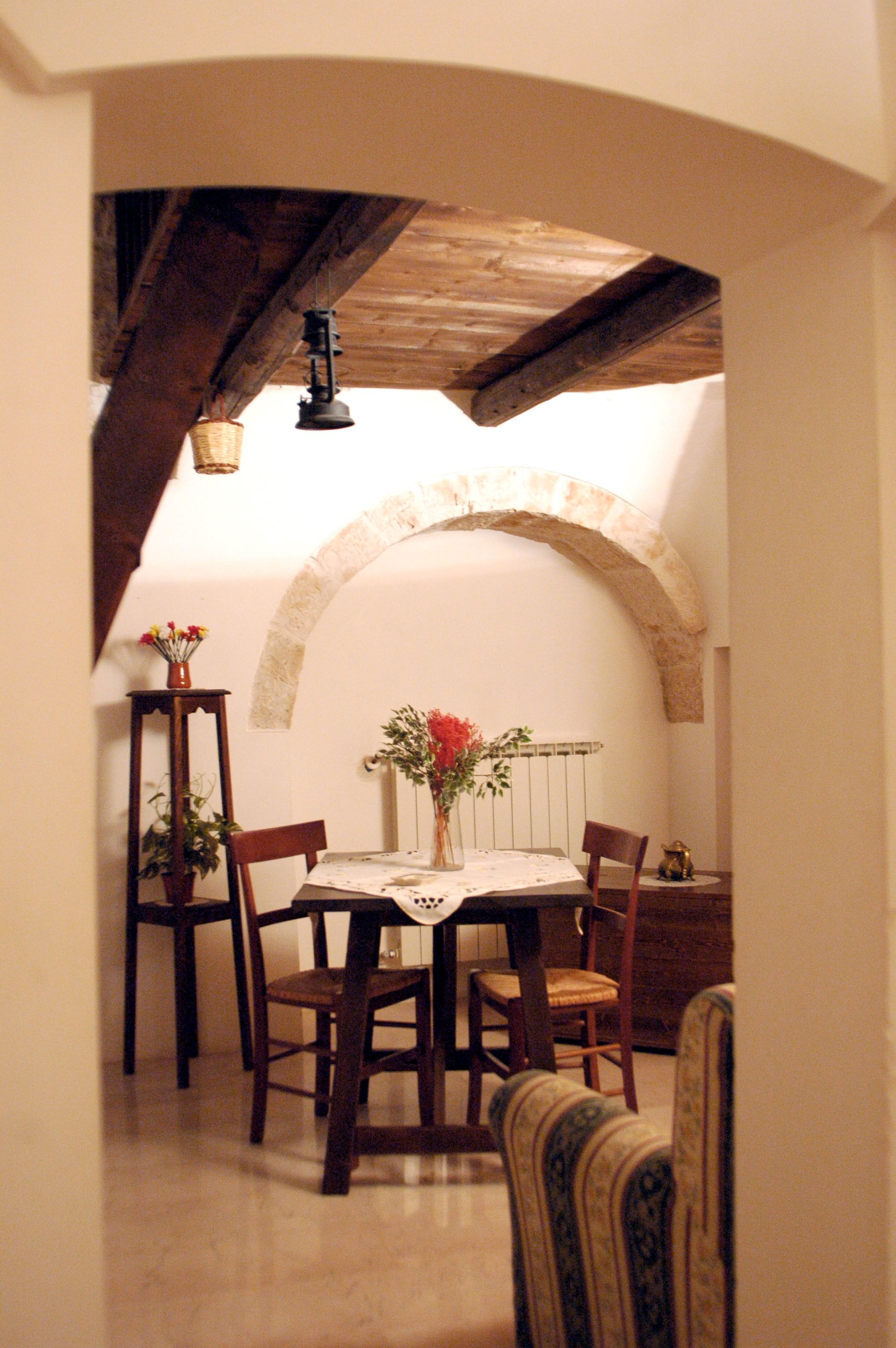 Comedor con una mesa dispuesta para cuatro personas, rodeado de sillas de madera, bajo un arco de piedra.