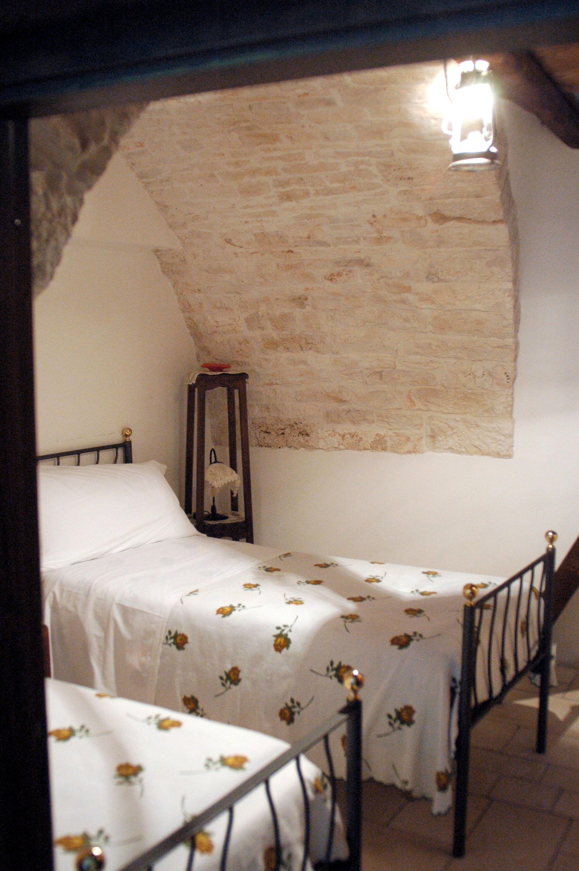Una habitación pequeña y rústica con dos camas individuales, una mesita de noche de madera y una pared de piedra.