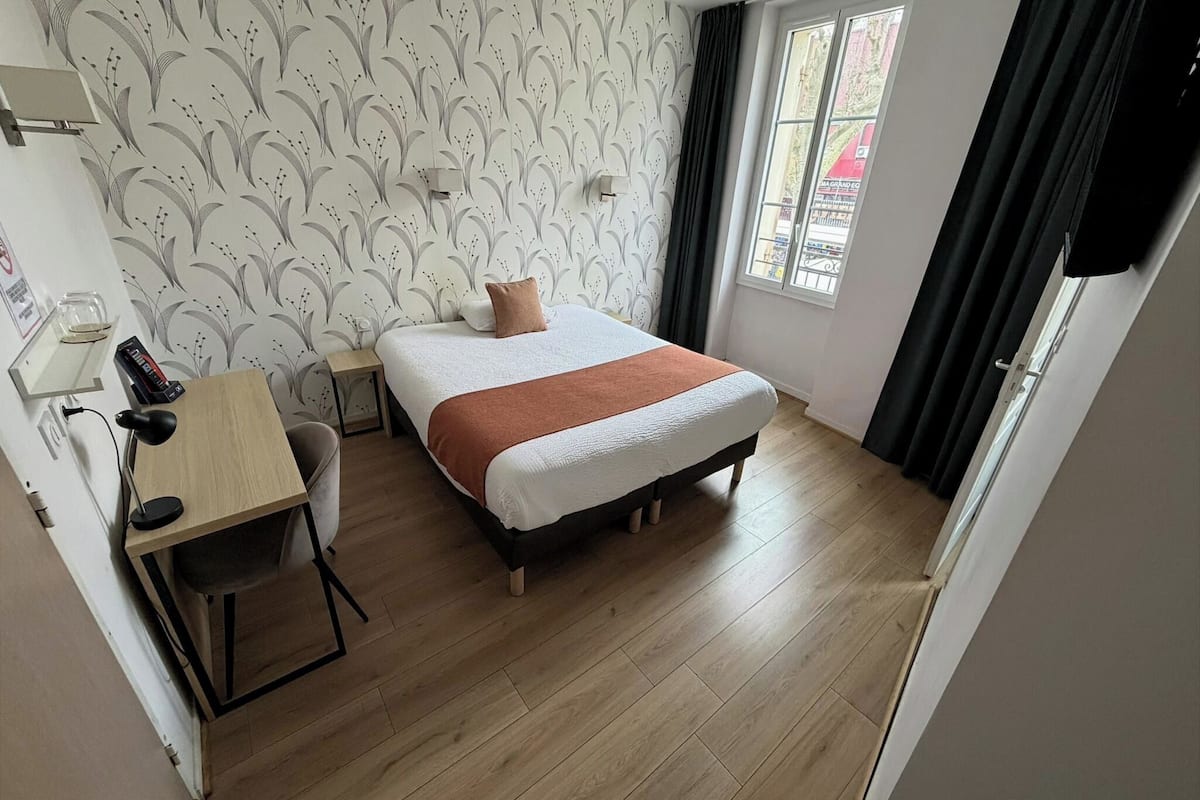 Ein Schlafzimmer mit Bett, Schreibtisch, Stuhl und einem Fenster mit Vorhängen.