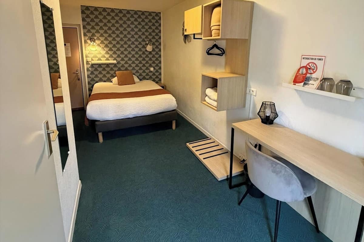 Ein kleines Hotelzimmer mit Bett, Schreibtisch und integrierten Regalen.
