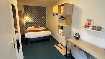Quarto de hotel compacto com cama, escrivaninha e prateleiras embutidas.