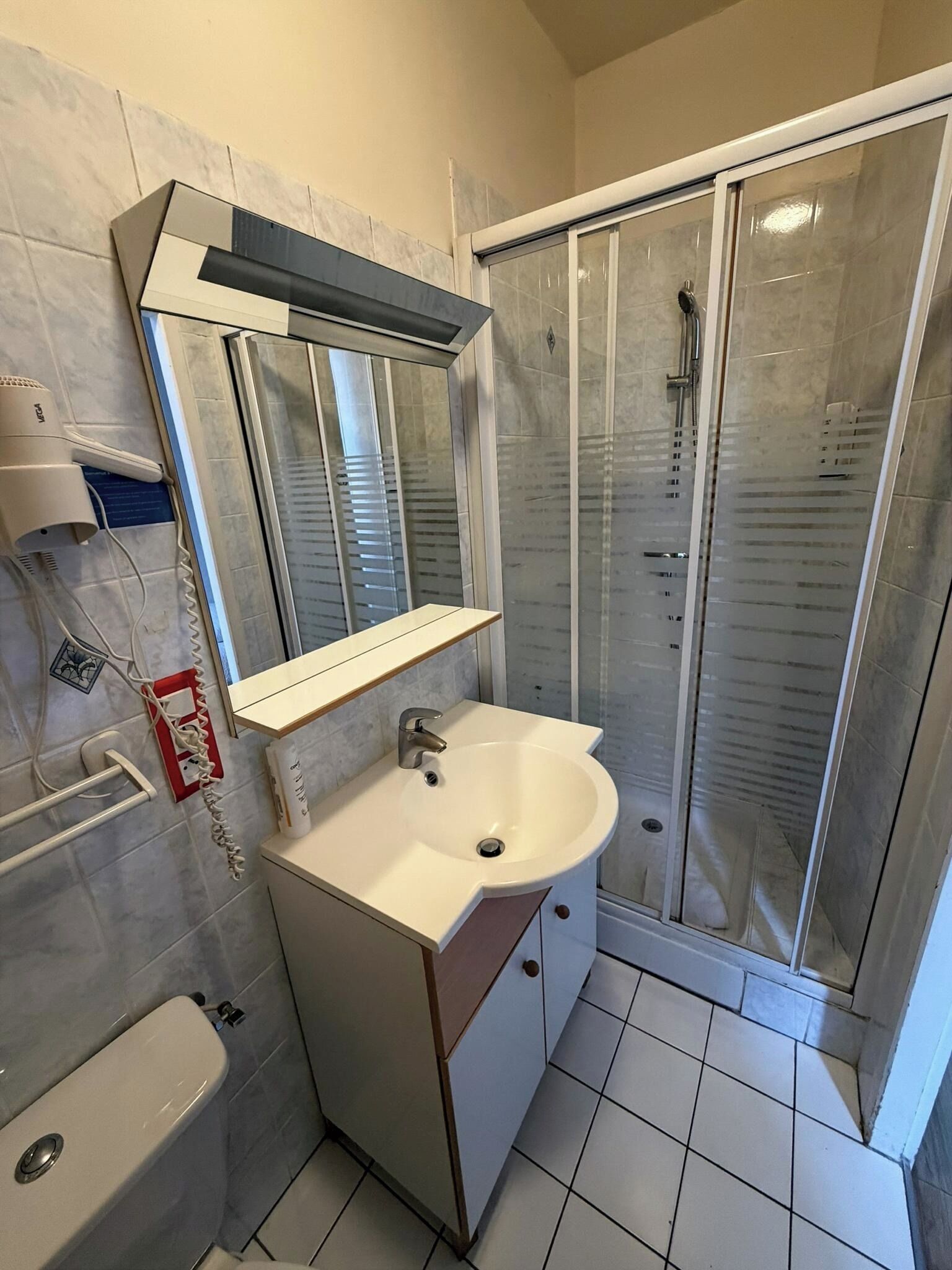 A bathroom with a sink, mirror, and shower enclosure.