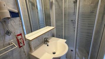 A bathroom with a sink, mirror, and shower enclosure.