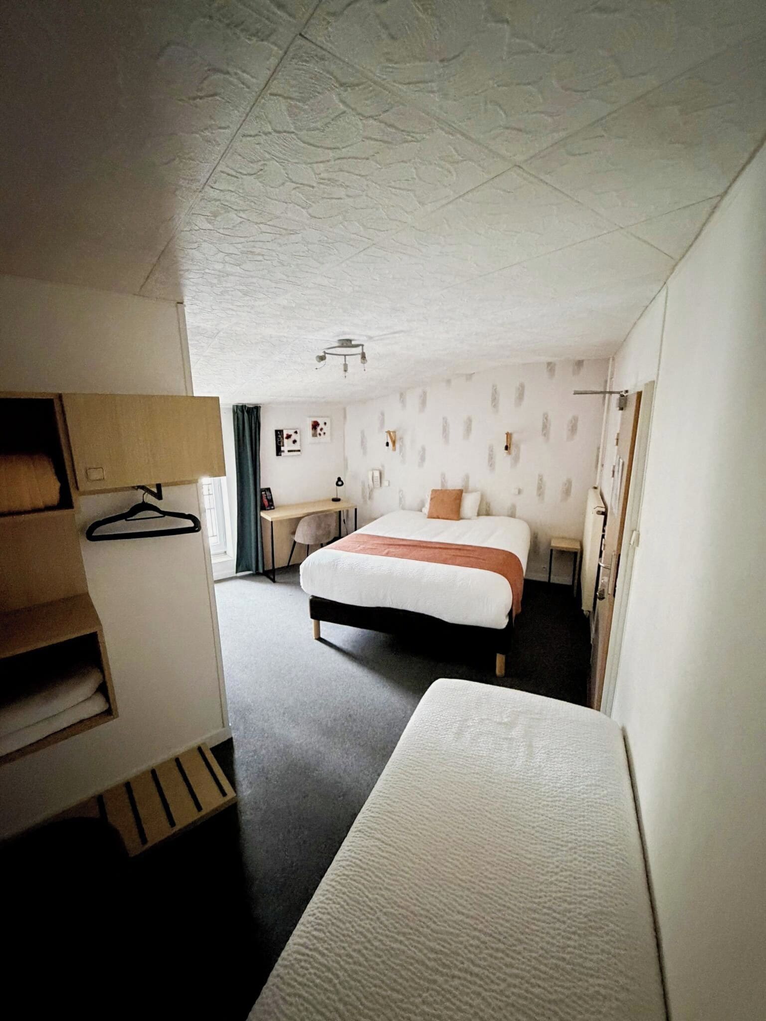 Een moderne hotelkamer met een groot bed, een nachtkastje, een kledingkast en een plafond met een reliëf patroon.