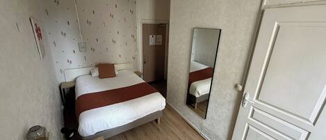 A hotel room with a bed, a desk, a chair, a mirror, and a door.