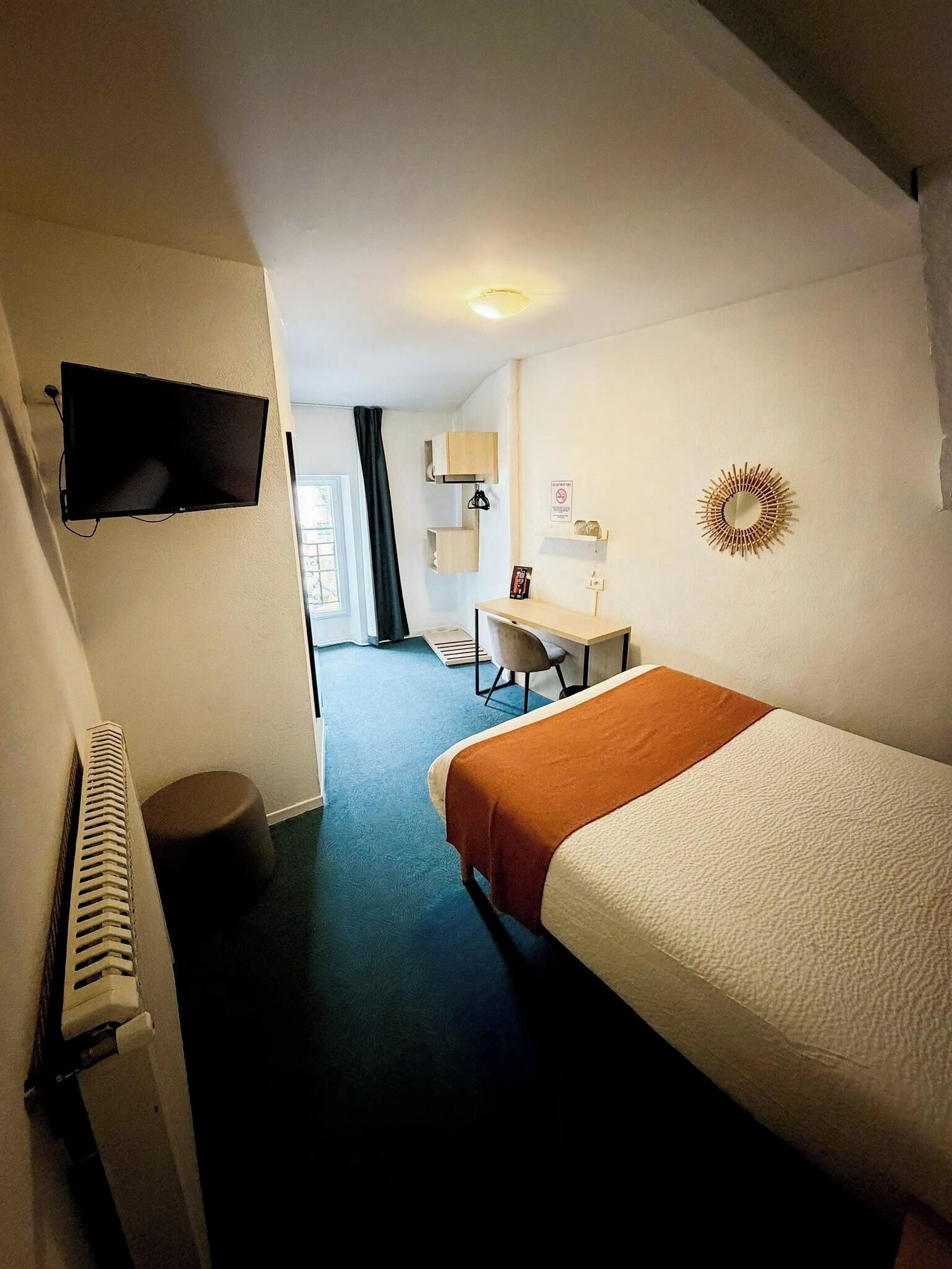A hotel room with a bed, a desk, a chair, a TV, and a radiator.