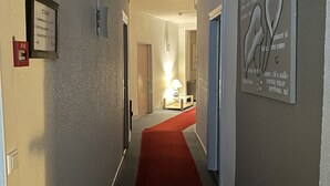 A hotel hallway with a red carpet, a framed sign on the left, and a wall art piece on the right. -  Contact Hôtel les Platanes Villeneuve sur Lot Centre (Villeneuve-sur-Lot)