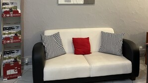 A modern living room with a white sofa, black and white patterned cushions, and a red accent pillow. A framed abstract painting hangs on the wall above the sofa. -  Contact Hôtel les Platanes Villeneuve sur Lot Centre (Villeneuve-sur-Lot)