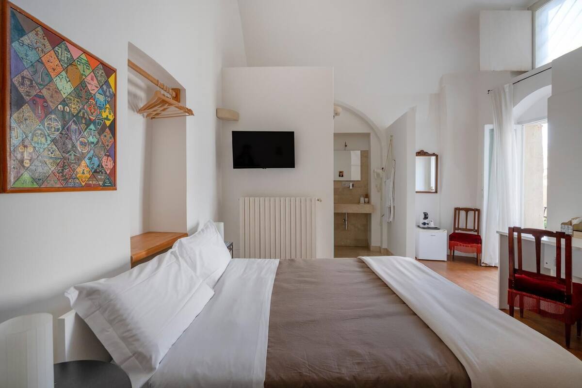 A modern bedroom with a bed, a TV, a radiator, a bathroom visible through an archway, and a red chair.