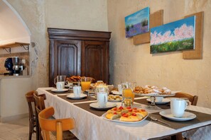 A breakfast table set with plates, cups, and a variety of pastries and bread, in a room with rustic decor and artwork on the walls. - La Corte Vetere (Matera)