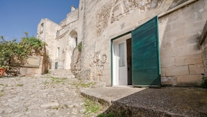 A stone building with a green door, a staircase leading to an upper level, and a small garden area with potted plants. - La Corte Vetere (Matera)
