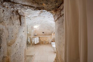 A narrow stone-walled bathroom with a shower, a toilet, and a bathtub. - La Corte Vetere (Matera)