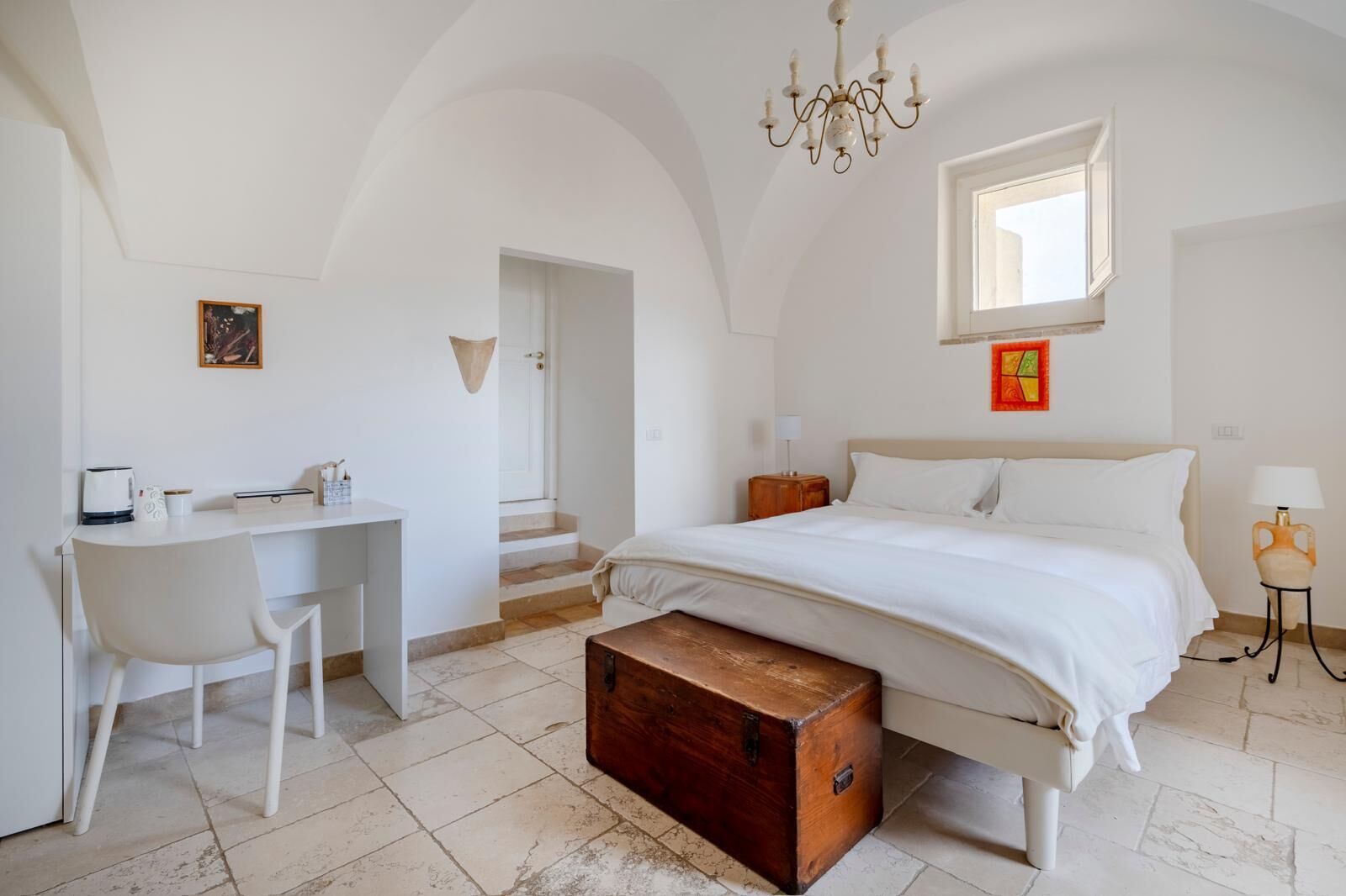 Une chambre à coucher comprenant un lit, un bureau, une chaise, une commode, un lustre et une fenêtre.