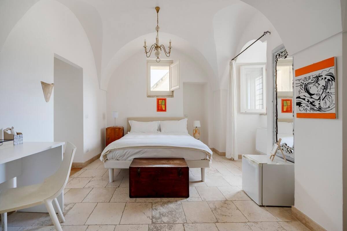 A bedroom with a bed, bedside tables, a desk, and a mirror.