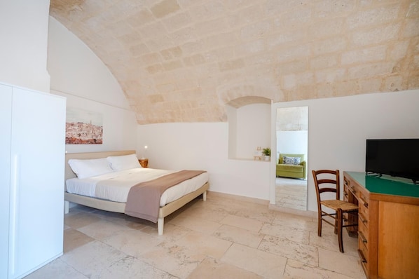 A bedroom with a bed, a desk with a chair, a TV, and a painting on the wall.