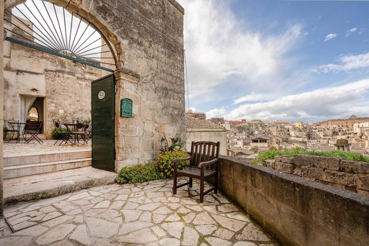A stone-paved patio with outdoor furniture, a green door, and a view of a historic cityscape.