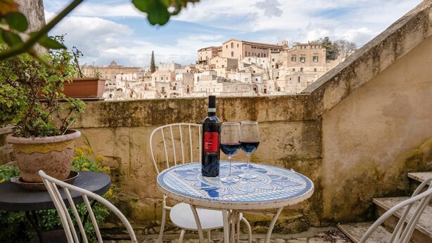 A table with a bottle of wine and two glasses on a tiled patio overlooking a cityscape. - La Corte Vetere (Matera)