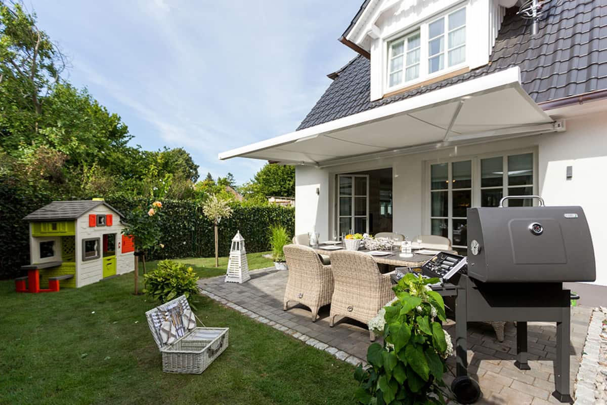 Een terras met tuinmeubilair, een barbecue en een speeltuintje.