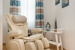 A massage chair with a control panel, a small table with a vase, and curtains.