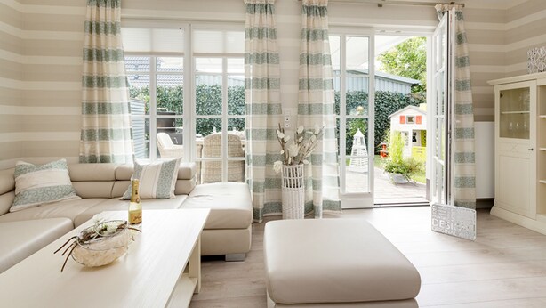 Uma sala de estar moderna com sofá, mesa de centro e área de refeições. Há uma janela grande com cortinas, vista para o exterior e um armário.