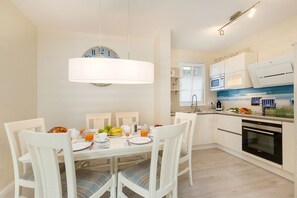 A modern kitchen with white cabinetry, a dining table with chairs, a clock, and a microwave.